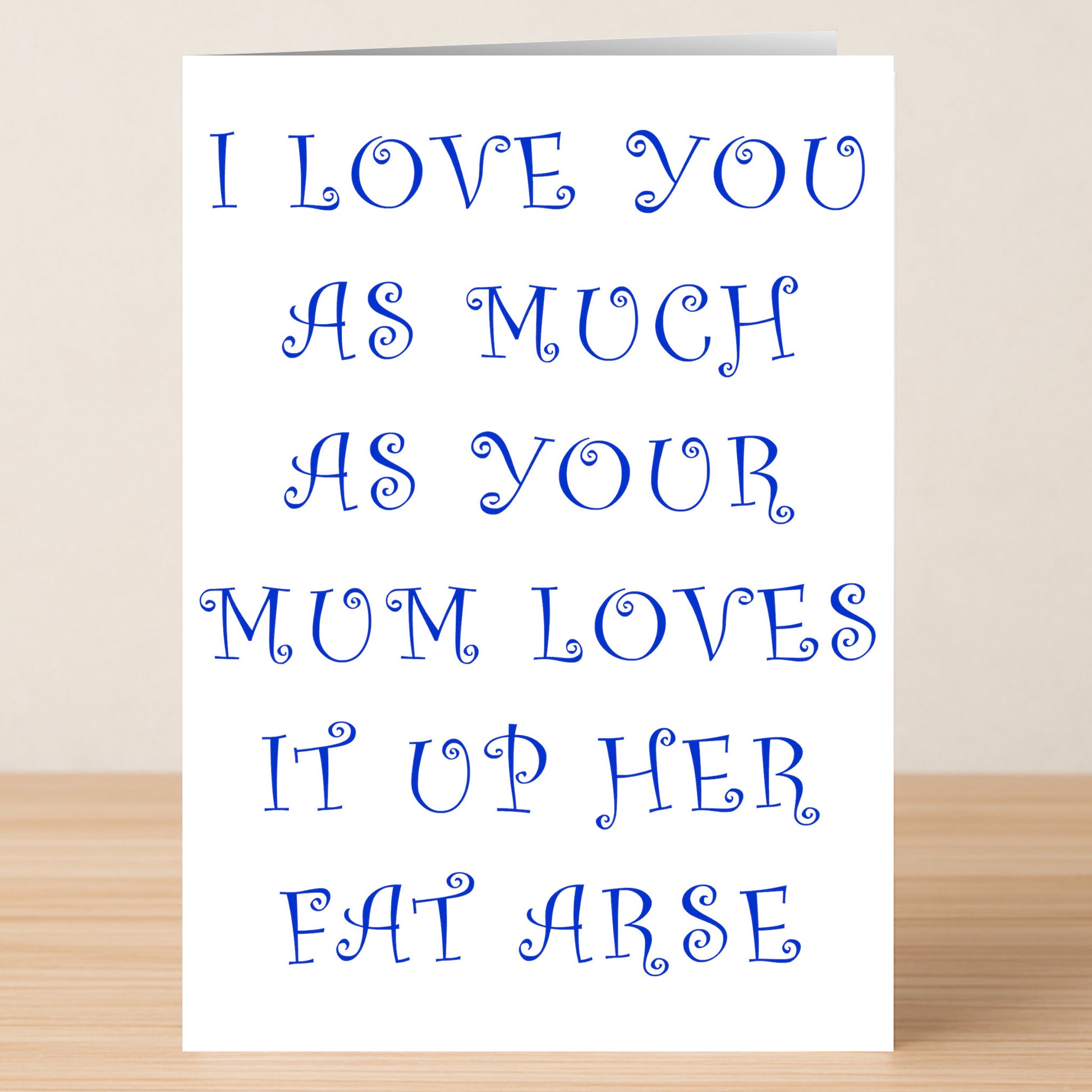 The Mum Rude Valentine's Card by Twisted Gifts sits on a wooden surface, humorously declaring in blue text, "I LOVE YOU AS MUCH AS YOUR MUM LOVES IT UP HER FAT ARSE"—the perfect unconventional Valentine’s gift.