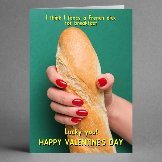 A hand adorned with red nails grips a baguette against a green background, accompanied by the text, "I think I fancy a French stick for breakfast. Lucky you! Happy Valentine's Day." This cheeky and playful card from Twisted Gifts is perfect for those who appreciate a humorous twist on romance—it's truly a delight in the form of the French Dick Rude Valentine's Card.