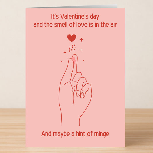 Twisted Gifts’ Love In The Air Rude Valentine's Card features a playful pink design with a sassy hand snap, heart above, and witty text humorously riffing on the scent of love—perfect for sharing laughs this Valentine’s Day.