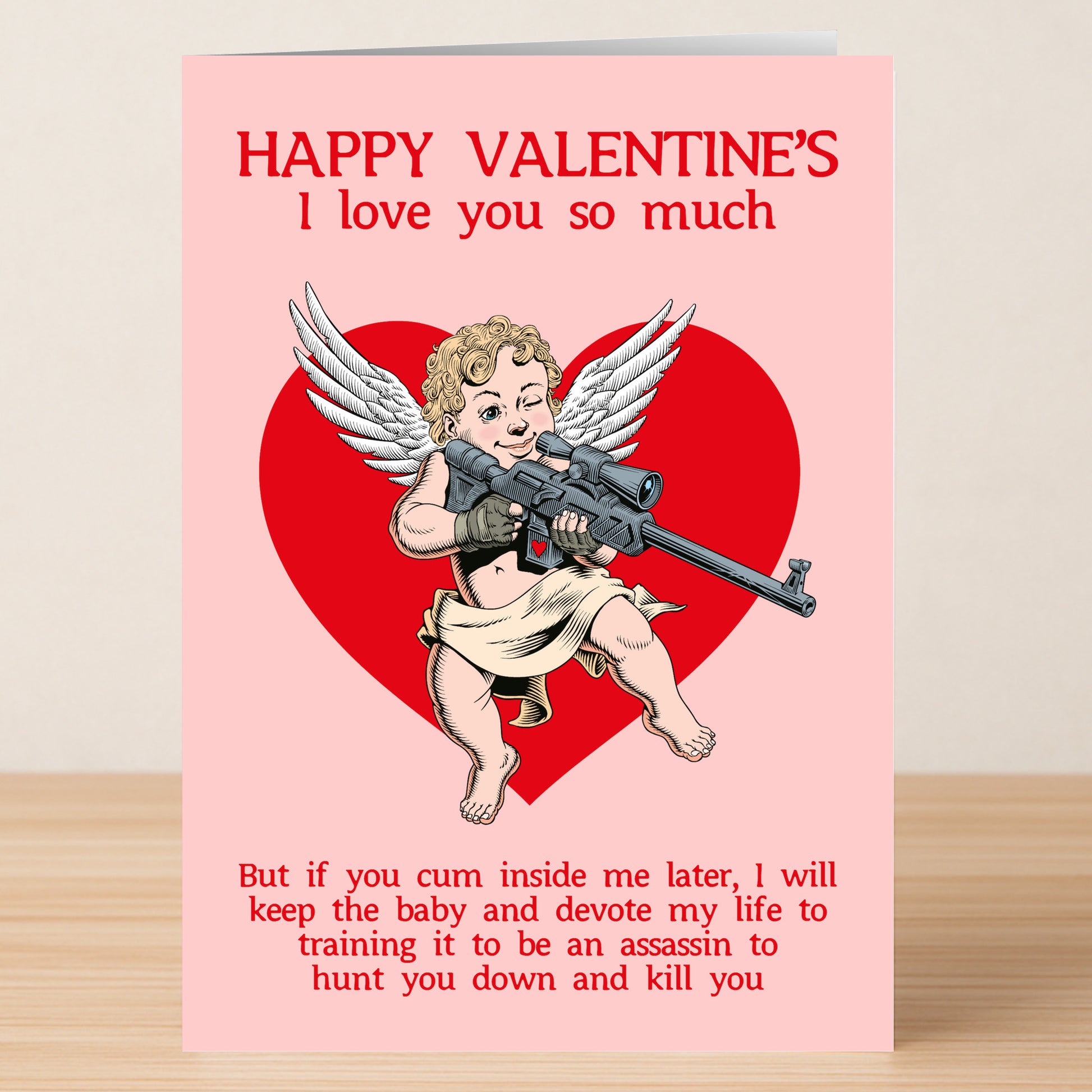 The Assassin Funny Valentine's Card by Twisted Gifts features a winged cherub with a sniper rifle in front of a red heart and witty, slightly threatening text—perfect for anyone with a playful sense of humor this Valentine’s Day.