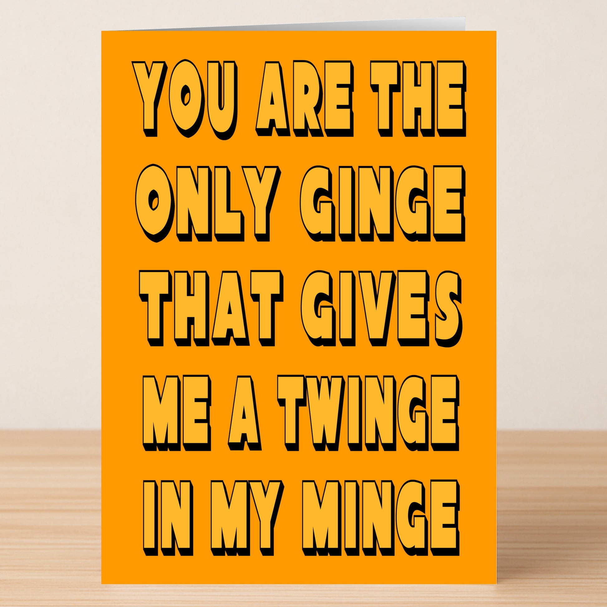 The Twinge Funny Valentine's Card by Twisted Gifts features bold black text on orange: "You are the only ginge that gives me a twinge in my minge." A perfect limited edition card for someone special, shown on a wooden surface.