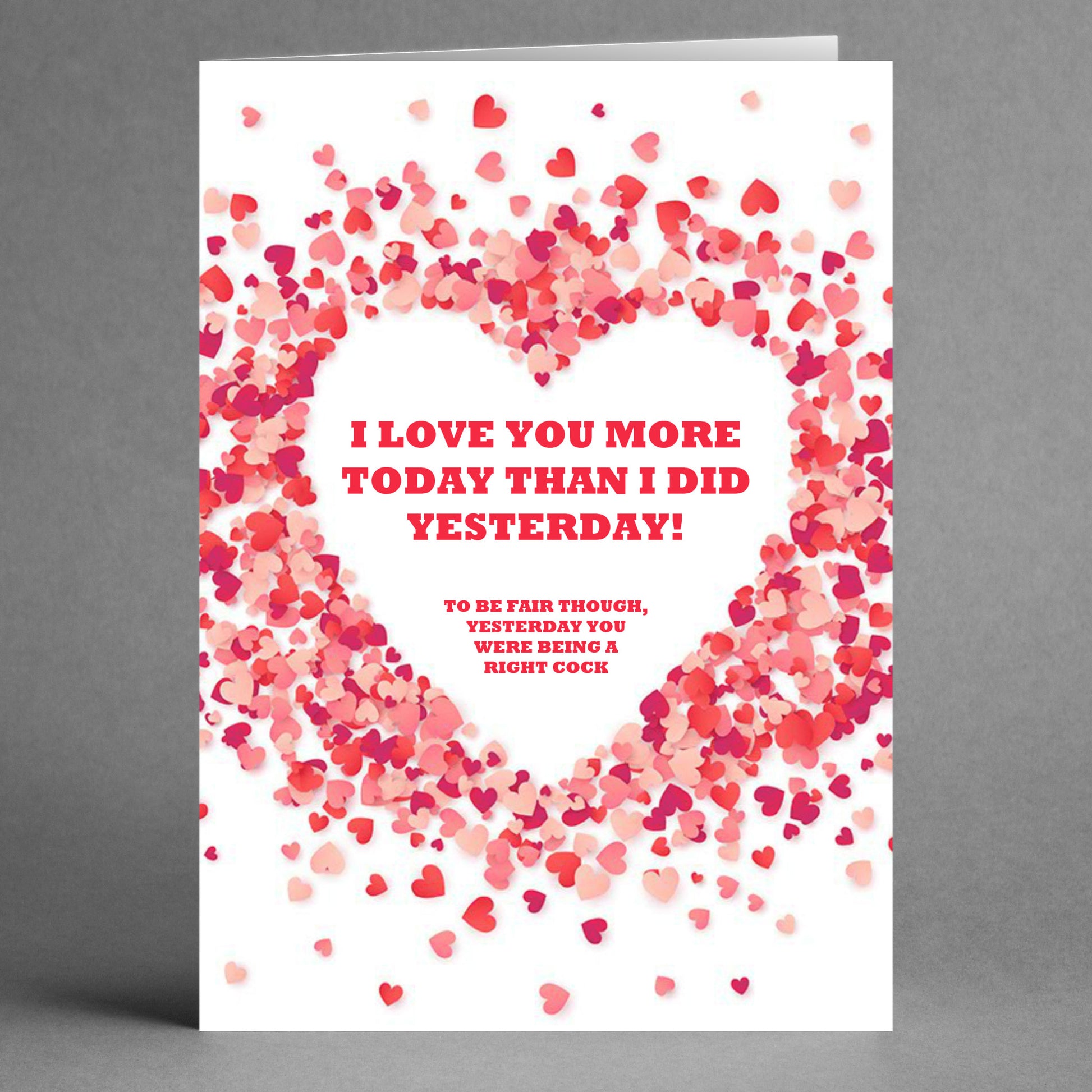 The Yesterday Funny Greeting Card from Twisted Gifts features a whimsical heart-shaped pattern with pink and red hearts. It includes the humorous message: "I love you more today than I did yesterday! To be fair though, yesterday you were being a right cock," promising to spark laughter and smiles.