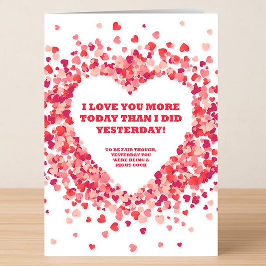 The Yesterday Funny Greeting Card by Twisted Gifts features pink and red heart confetti forming a heart and reads: "I love you more today than I did yesterday! To be fair though, yesterday you were being a right cock.
