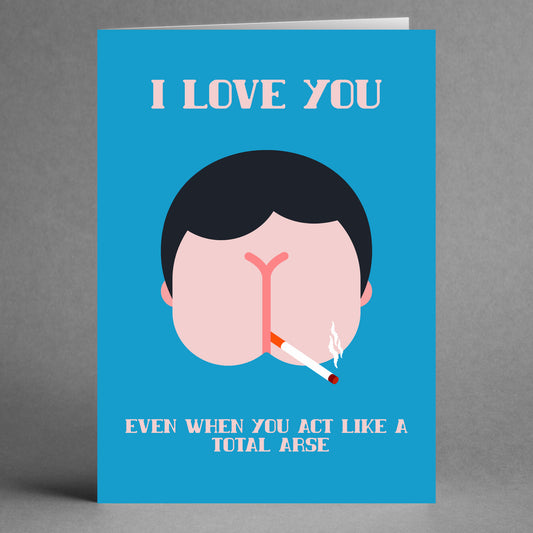 Introducing the Total Arse Insulting Greeting Card by Twisted Gifts, showcasing a quirky design of a person's head humorously shaped like an arse, complete with smoking a cigarette. The amusing message, "I LOVE YOU EVEN WHEN YOU ACT LIKE A TOTAL ARSE," stands out on a blue background, perfectly blending humor with affection.