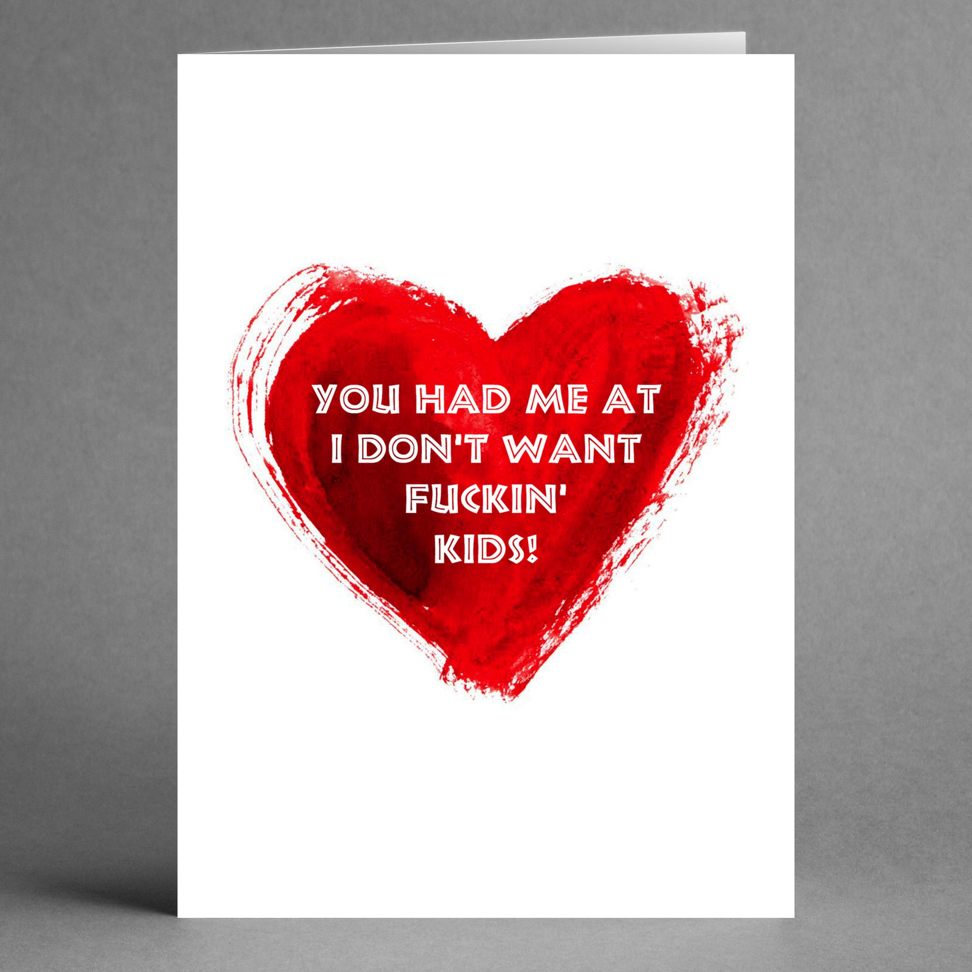 A white card featuring a red heart and the text, "You had me at I don't want fuckin' kids!" This one-of-a-kind Kids Funny Valentine's Card from Twisted Gifts is the ideal humorous greeting for those who value wit and straightforwardness in their relationships.