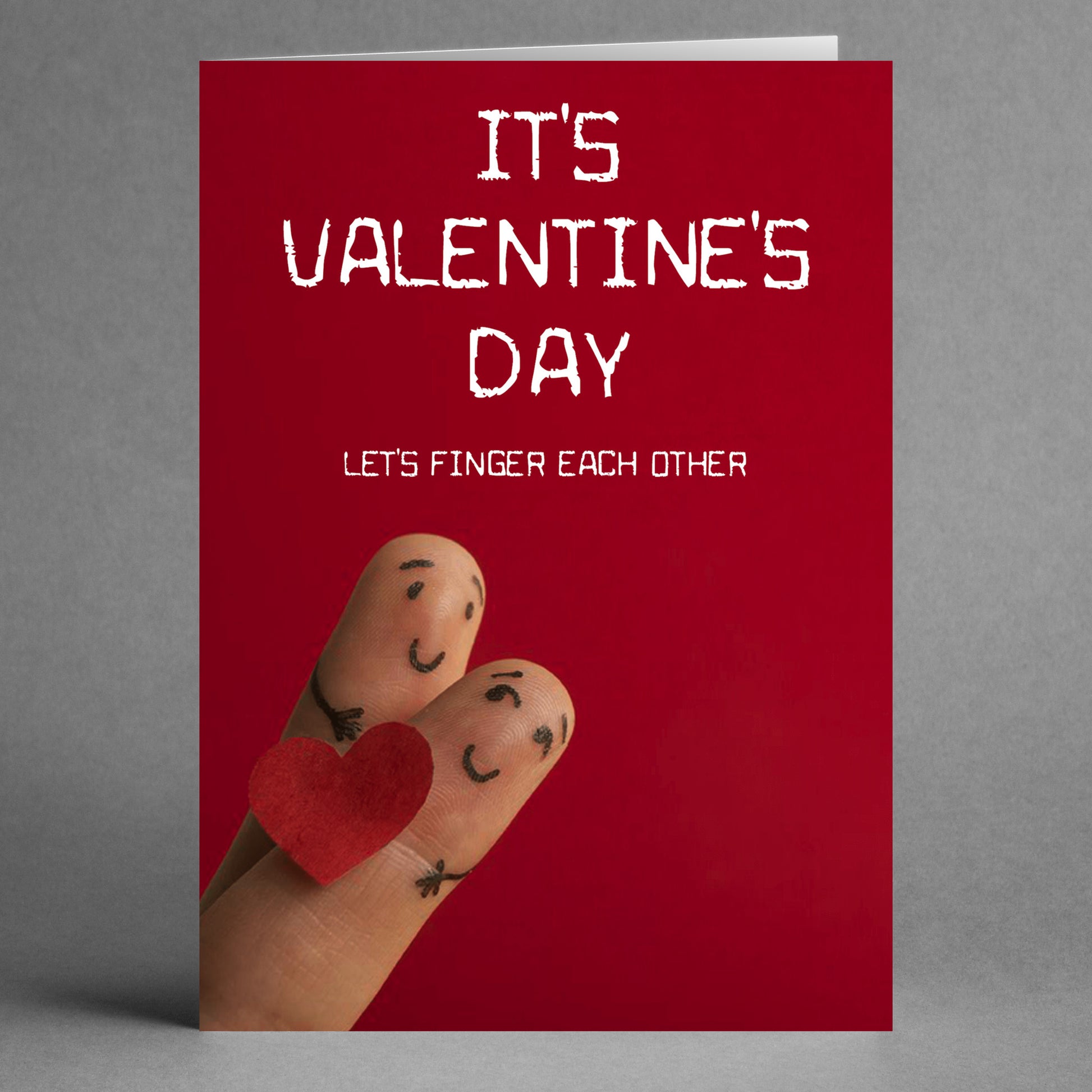 The Finger Rude Valentine's Card by Twisted Gifts showcases a humorous design with two fingers painted as happy faces holding a small red heart. The cheeky text on top humorously declares, "It's Valentine's Day. Let's finger each other." Ideal for those who enjoy a playful and cheeky twist on a Valentine’s card!