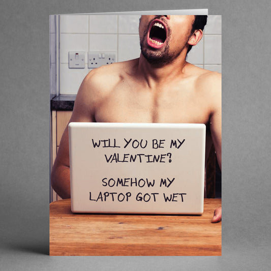 A man sits at a table, shirtless and with his mouth open, holding a sign that reads "Will you be my Valentine?", capturing the perfect quirky couple's vibe. Amidst this scene, his laptop got wet, adding a touch of chaos to this moment showcased on the Twisted Gifts' product: Wet Laptop Rude Valentine's Card.