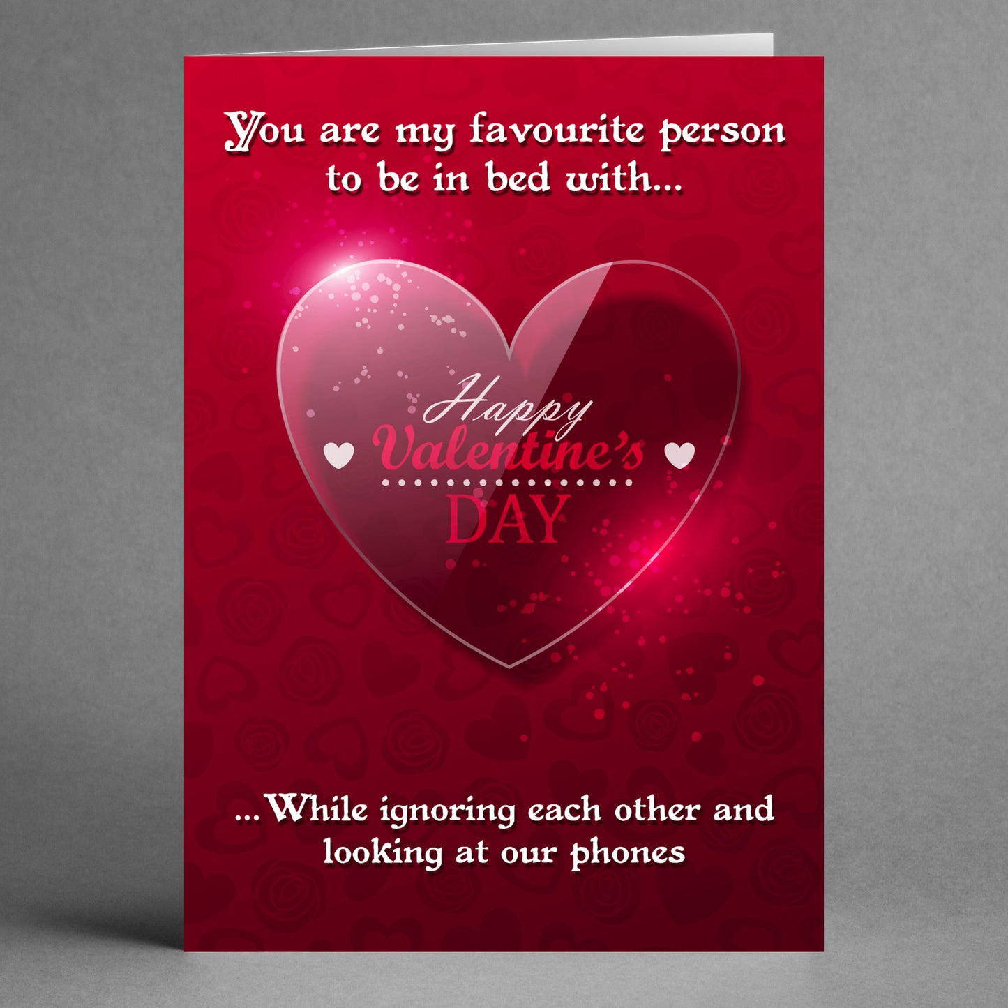 The Phones Funny Valentine's Card by Twisted Gifts features a red design with a glossy heart, white text, and a playful techy love message about being in bed while ignoring each other and using phones. It captures the essence of modern romance with a humorous twist.