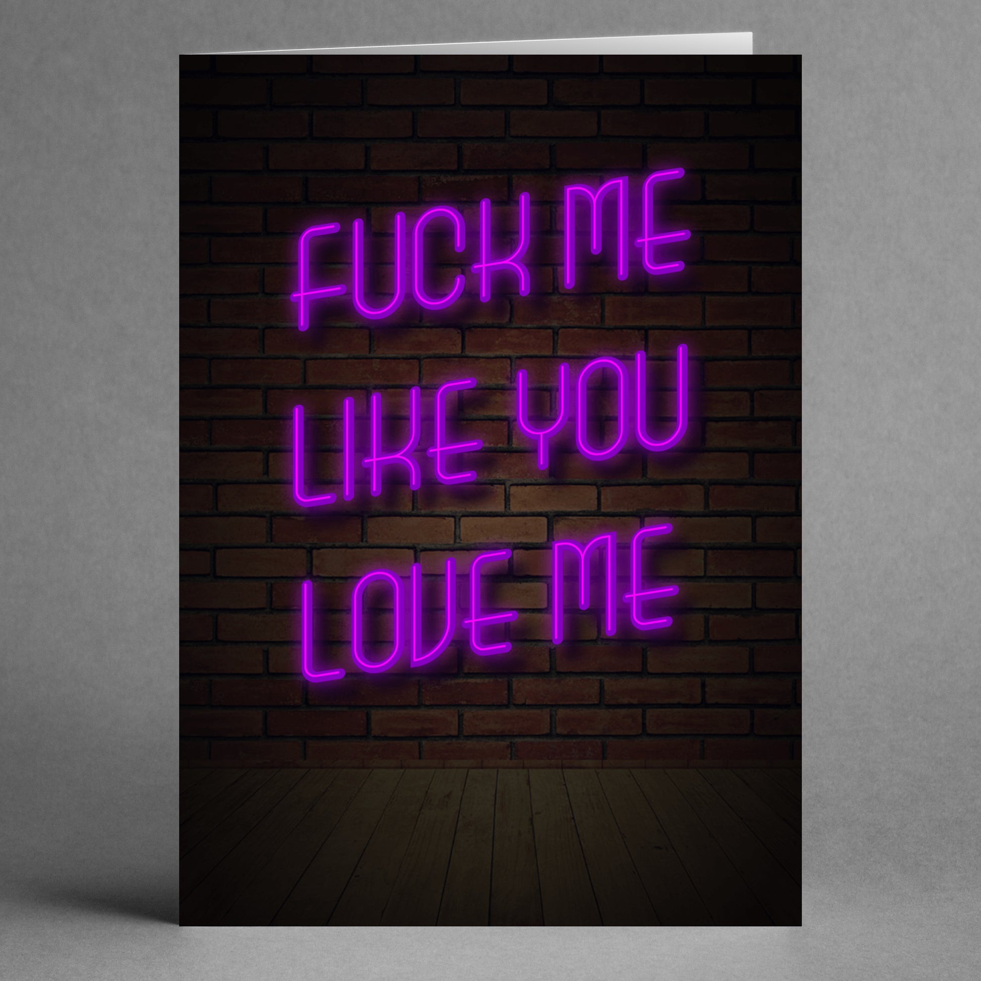 A cheeky neon sign on a brick wall reads, "Fuck me like you love me," bringing the audacious humor of Twisted Gifts' "Like You Love Me" Rude Valentine's Card to life.