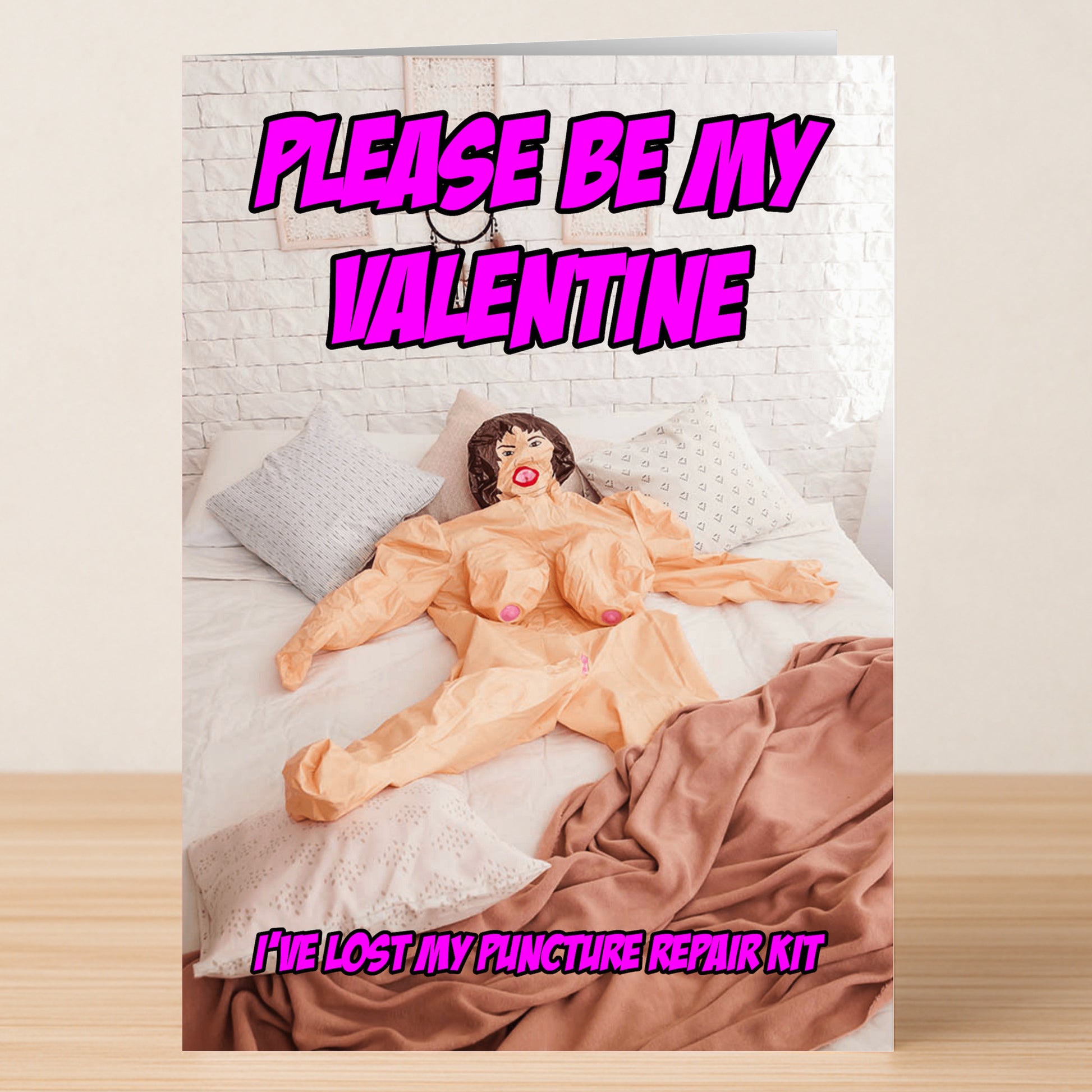 The Repair Kit Rude Valentine's Card from Twisted Gifts features a blow-up doll on a bed with pillows and blanket, plus the text "PLEASE BE MY VALENTINE. I'VE LOST MY REPAIR KIT." It's the perfect sarcastic card for Valentine's Day!.