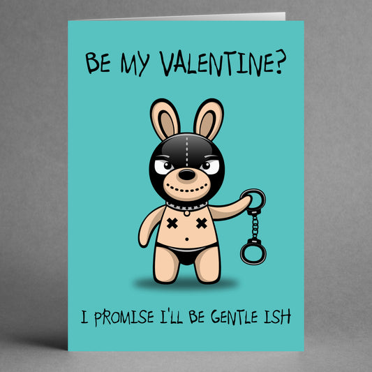 The "Gentle Ish Rude Valentine's Card" by Twisted Gifts showcases a cartoon bunny in a bondage mask holding handcuffs, accompanied by the text "Be my Valentine? I promise I'll be gentle-ish" on a teal background. Ideal for those who enjoy sarcasm and wit!