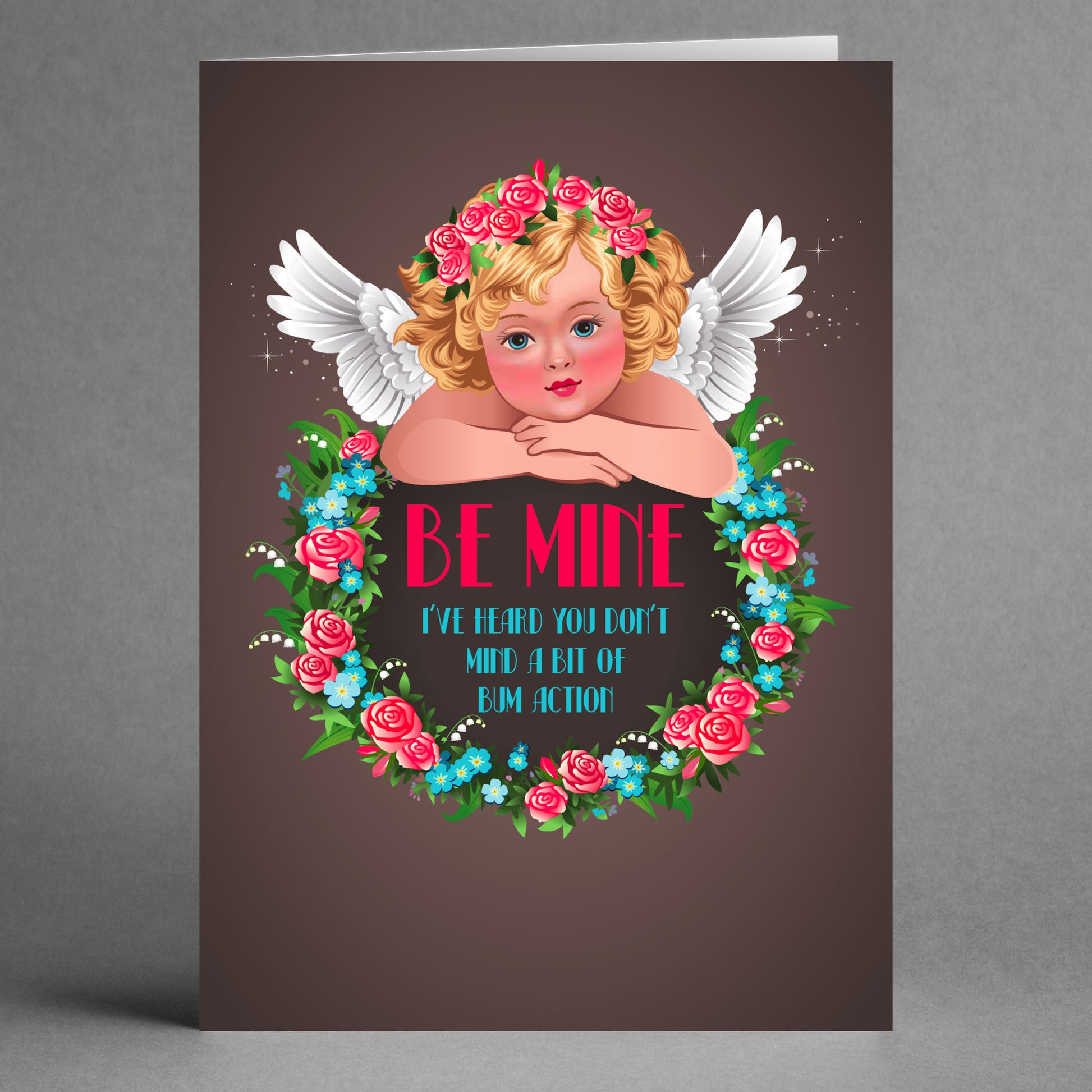 Twisted Gifts presents the Action Rude Valentine's Card, an imaginative greeting featuring a cherub with wings encircled by a floral wreath, complete with the playful text "Be Mine - I've heard you don't mind a bit of bim action." Perfect for those who enjoy an unconventional touch.