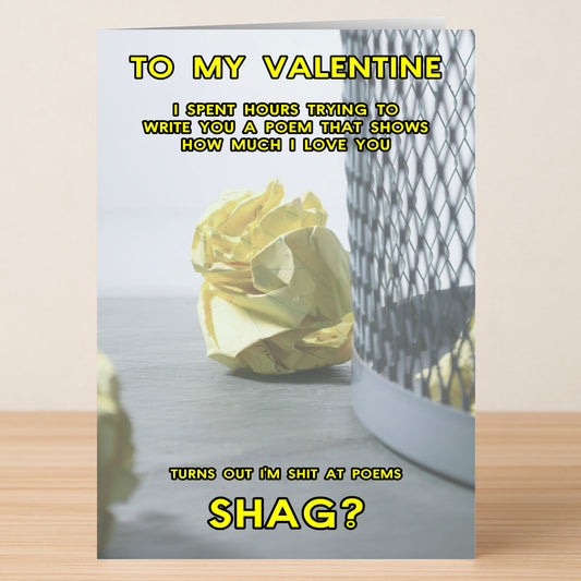 A crumpled yellow paper beside a wastebasket on a wooden table, with witty yellow text about writing a clever poem for the Twisted Gifts Poem Funny Valentine's Card.