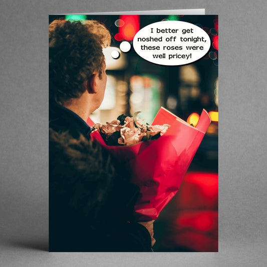 A person holds a bouquet of pink roses, with a thought bubble reading, "I better get noshed off tonight, these roses were well pricey!" The moment humorously reflects the card's intention from Twisted Gifts' "Pricey Insulting Valentine's Card," set against the backdrop of blurred city lights.