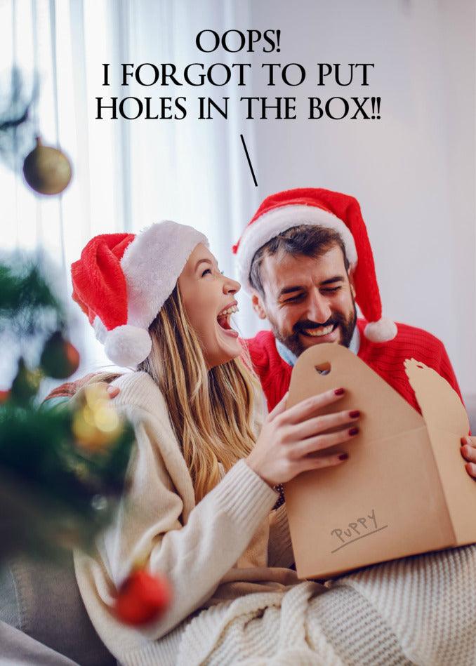 A couple in Santa hats is opening a box with No Holes Funny Christmas Card from Twisted Gifts inside, creating a funny Christmas card moment.