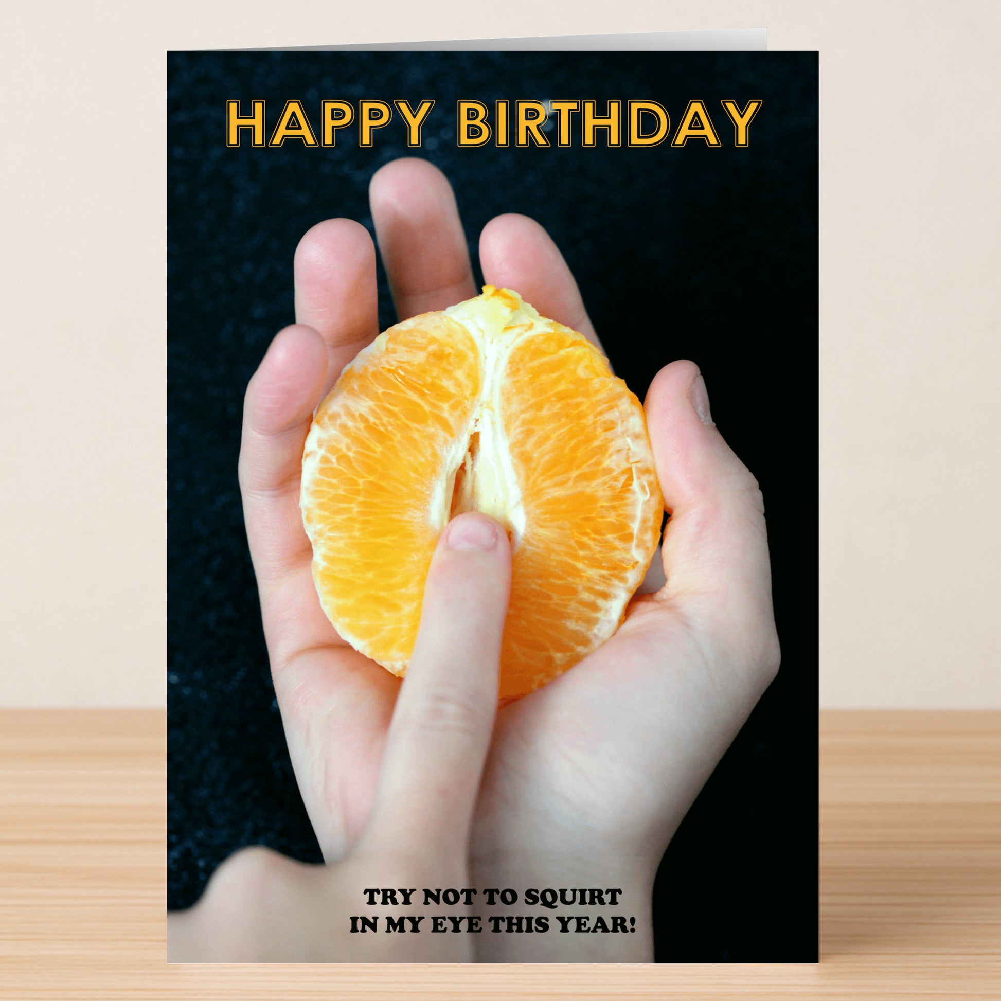 A hand squeezes a halved orange on the Squirt Rude Birthday Card by Twisted Gifts. "Happy Birthday" appears at the top; below is "Try not to squirt in my eye this year!"—a funny card for those who love a cheeky sense of humor.