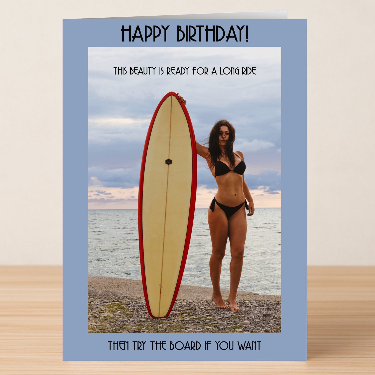 A woman in a bikini stands on the beach holding a surfboard upright, featured on Twisted Gifts' "Ready For A Ride – Rude Birthday Card" with funny text above and below.