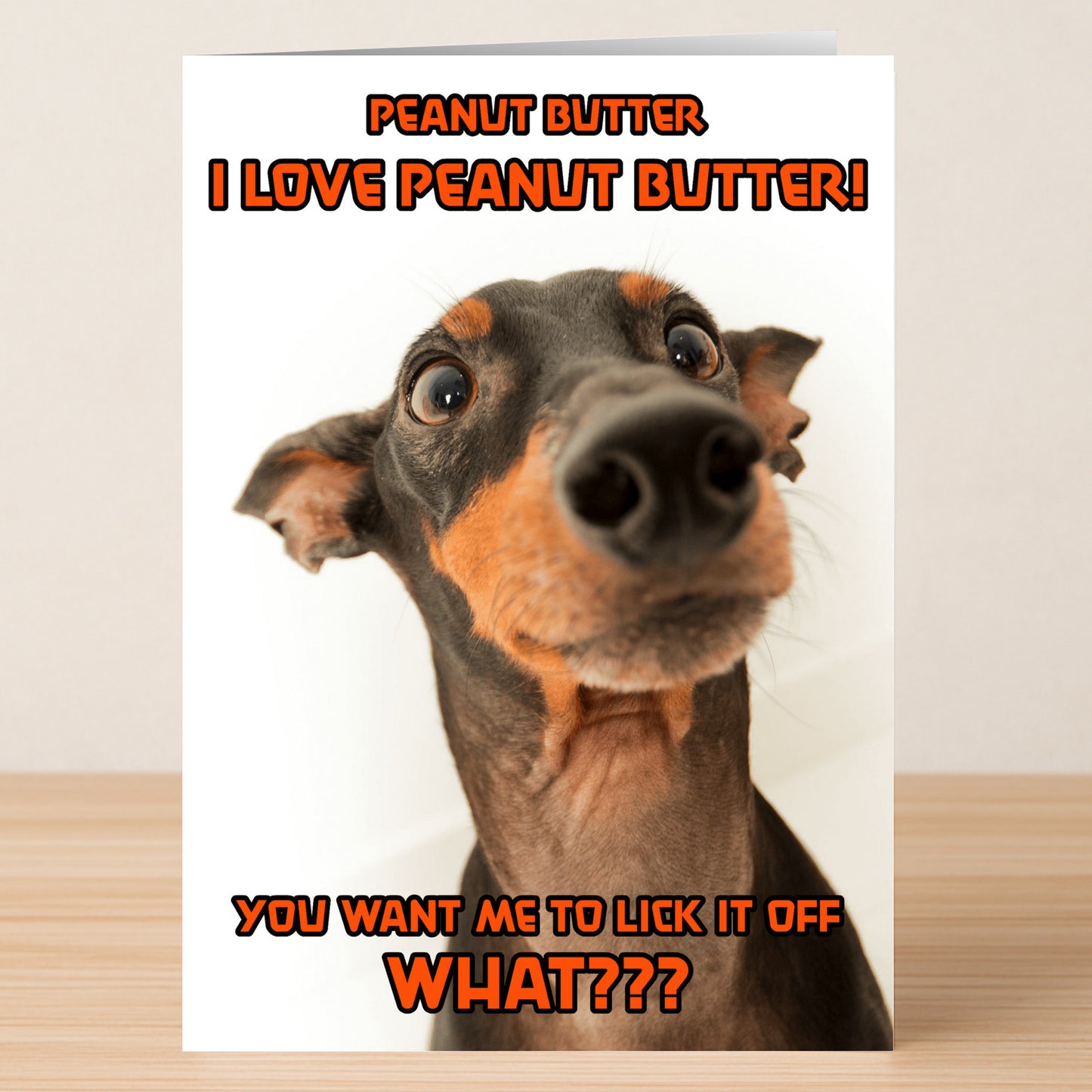 The Peanut Butter – Funny Birthday Card by Twisted Gifts features a close-up of a curious Doberman and orange text: “PEANUT BUTTER I LOVE PEANUT BUTTER! YOU WANT ME TO LICK IT OFF WHAT???”.