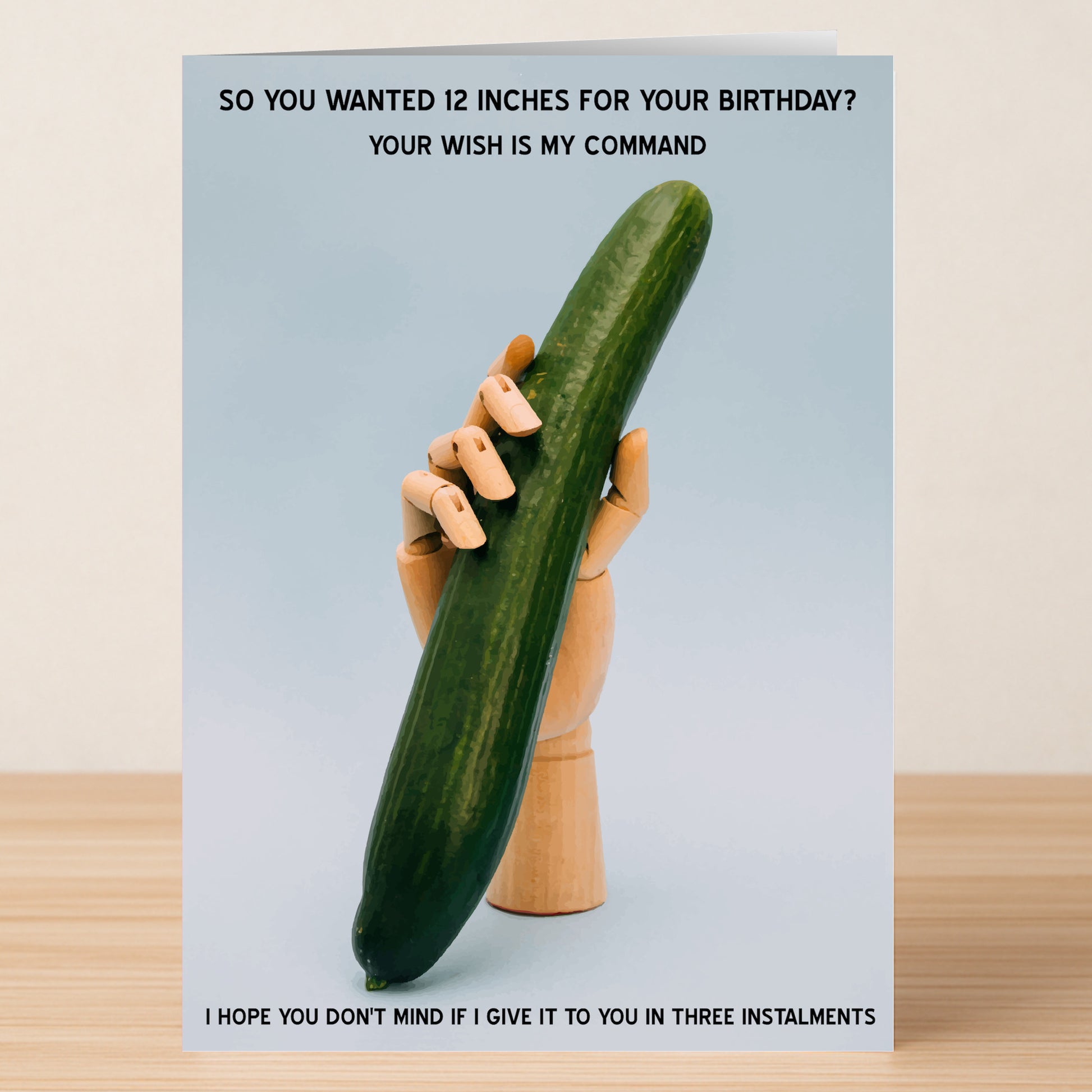 The Twisted Gifts "Instalments – Rude Birthday Card" features a wooden mannequin hand holding a large cucumber upright against a blue background, with joke text about fulfilling birthday wishes in installments.