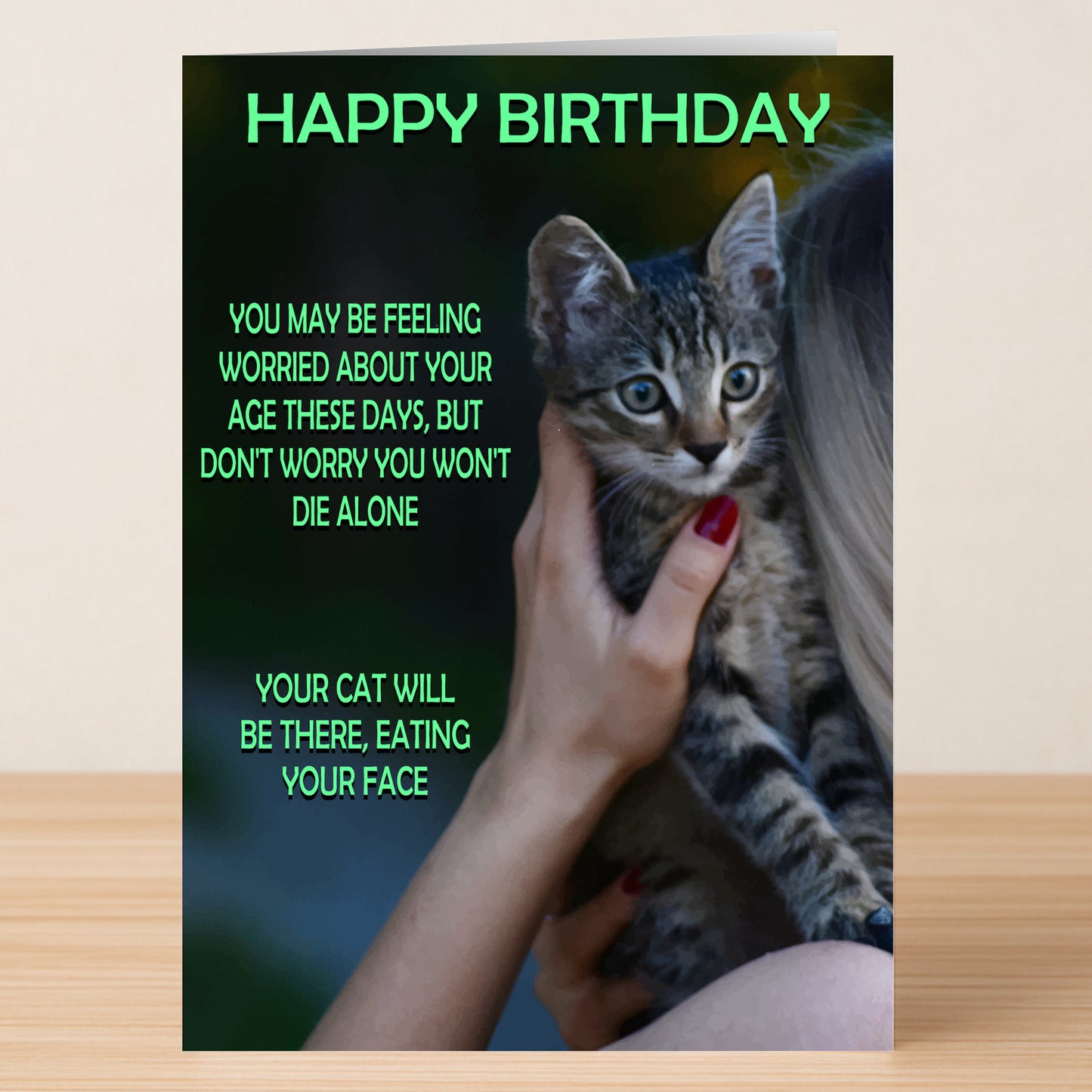 A person holds a tabby kitten and the "Die Alone – Dark Humour Birthday Card" from Twisted Gifts, which features a funny, slightly rude message about aging and a cat eating their face.