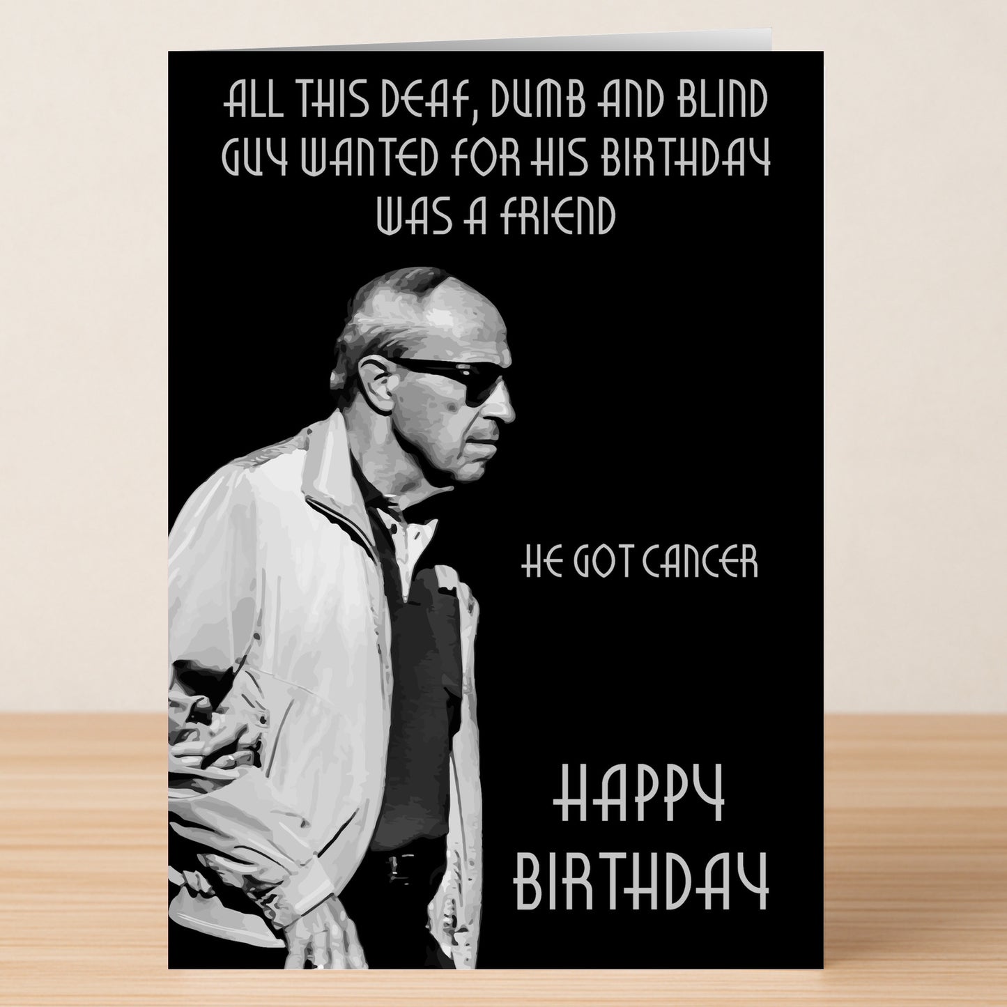 The “All He Wanted – Dark Humour Birthday Card” by Twisted Gifts features a black-and-white design with an older man in sunglasses and the cheeky birthday message: “All this deaf, dumb, and blind guy wanted for his birthday was a friend. He got cancer.”.