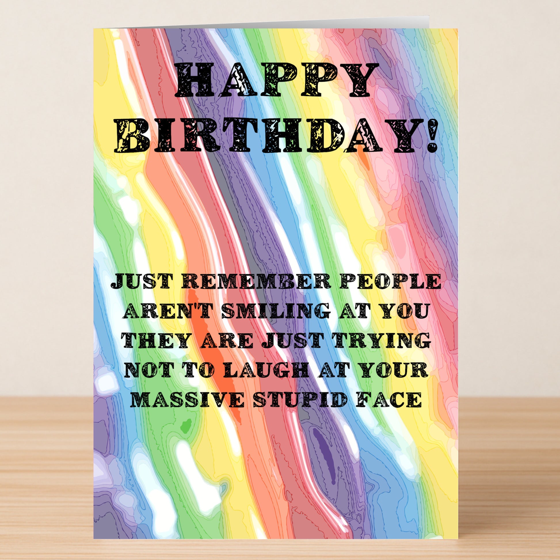 The Stupid Face – Insulting Birthday Card by Twisted Gifts features rainbow swirls and the message: "HAPPY BIRTHDAY! Just remember people aren't smiling at you—they're just trying not to laugh at your massive stupid face.