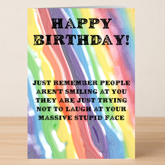 The Stupid Face Insulting Birthday Card by Twisted Gifts features a colorful wavy rainbow design and black text: "HAPPY BIRTHDAY! Just remember people aren't smiling at you—they're trying not to laugh at your massive stupid face.