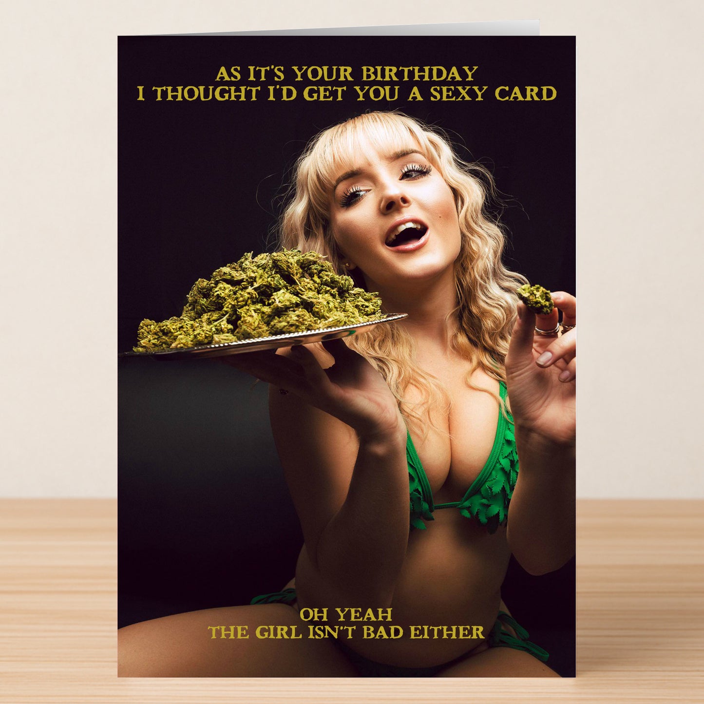 A woman in a green bikini holds cannabis buds on the Sexy – Funny Birthday Card by Twisted Gifts, which reads, "As it's your birthday I thought I'd get you a sexy card. Oh yeah, the girl isn't bad either.