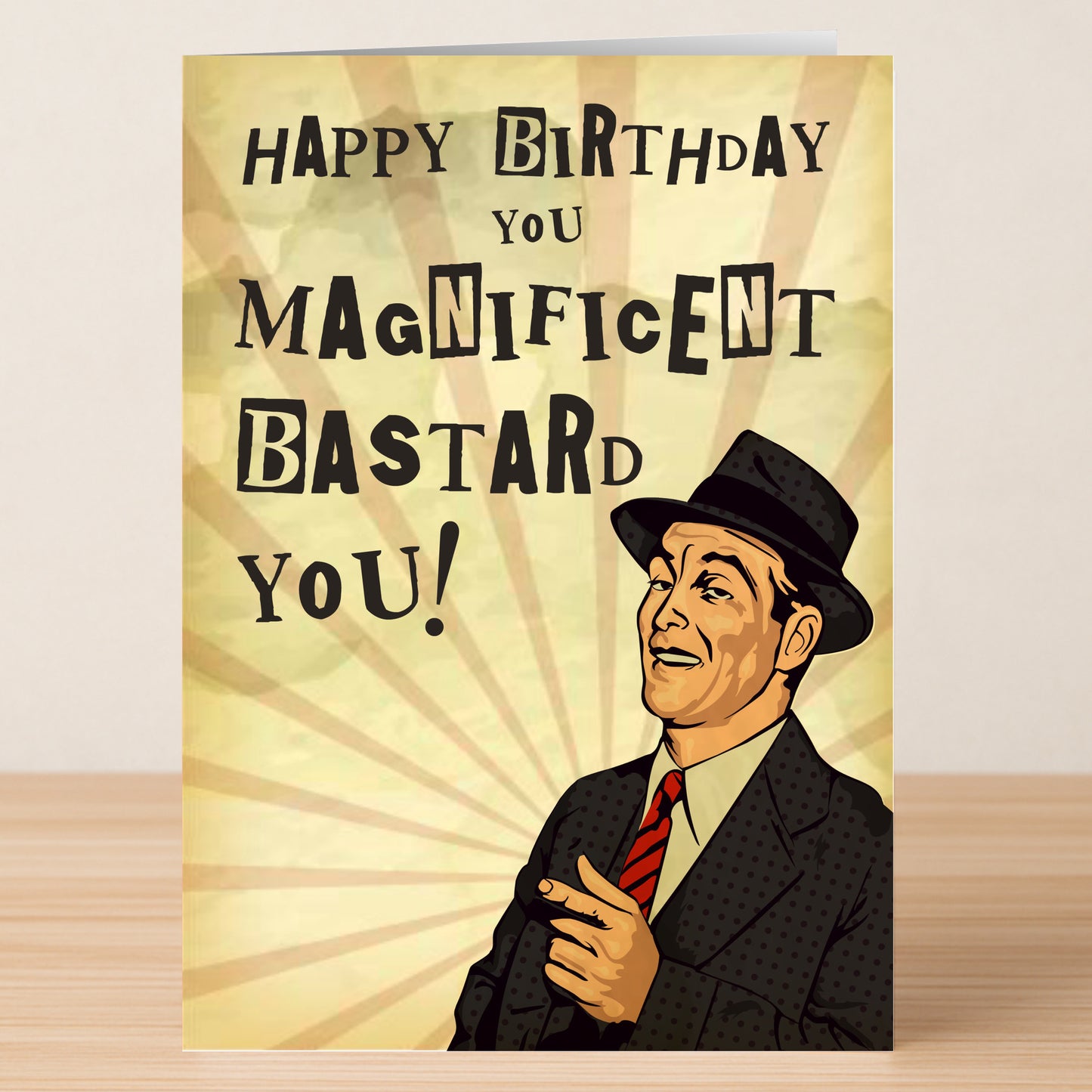 The Magnificent Bastard – Funny Birthday Card by Twisted Gifts features a vintage illustration of a man in a suit and hat pointing, with the message, "Happy Birthday you magnificent bastard you!" displayed on a wooden surface.