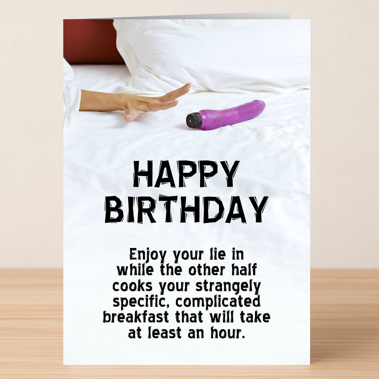 A hand reaches for a purple vibrator on a bed above the text: "HAPPY BIRTHDAY. Enjoy your lie in while the other half cooks your strangely specific, complicated breakfast." Twisted Gifts' Lie In – Rude Birthday Card is perfect for anyone with a wicked sense of humor.