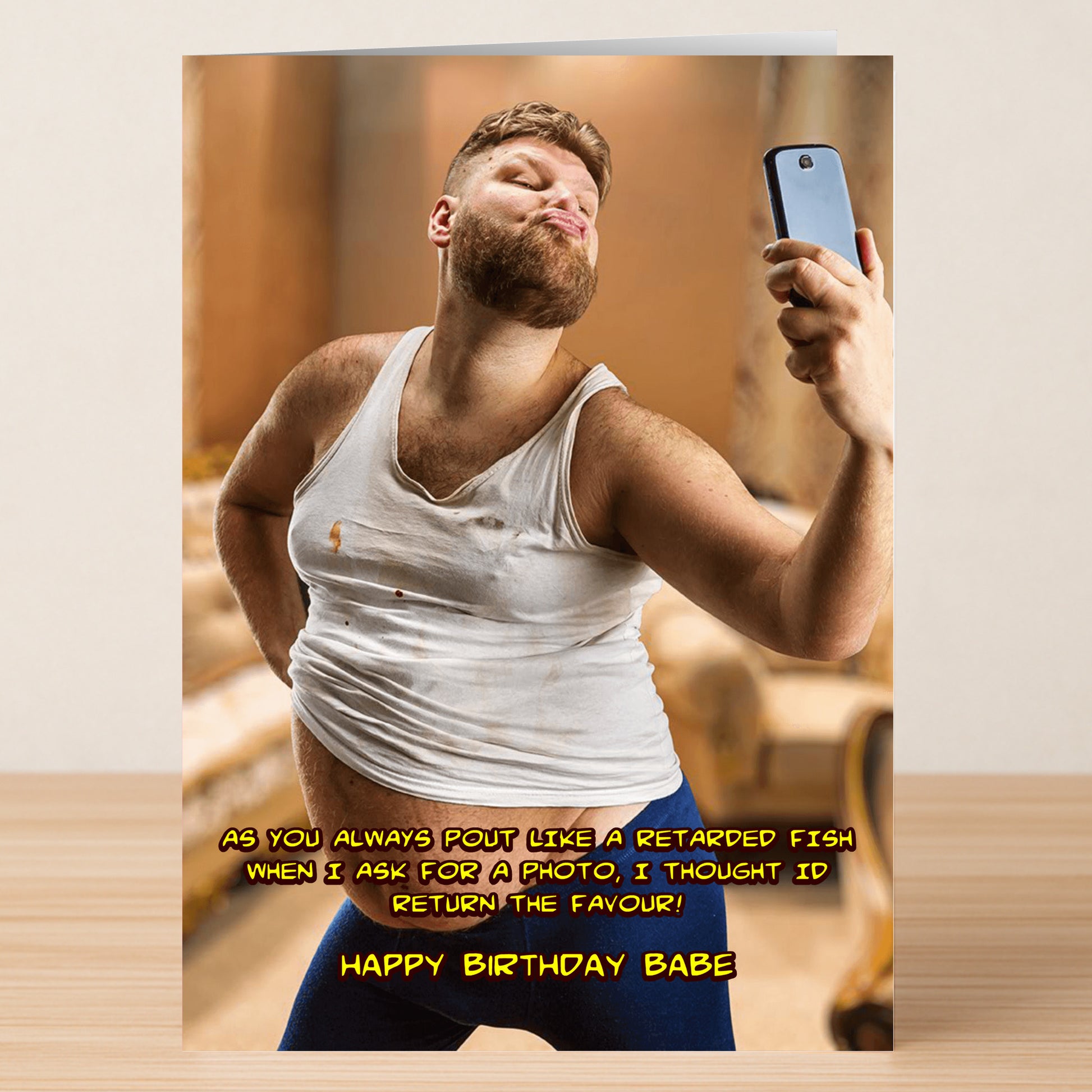 A bearded man in a ripped white tank and blue pants pouts for a selfie indoors on the Fish – Funny Birthday Card by Twisted Gifts, featuring "Happy birthday babe" with a humorous message above.
