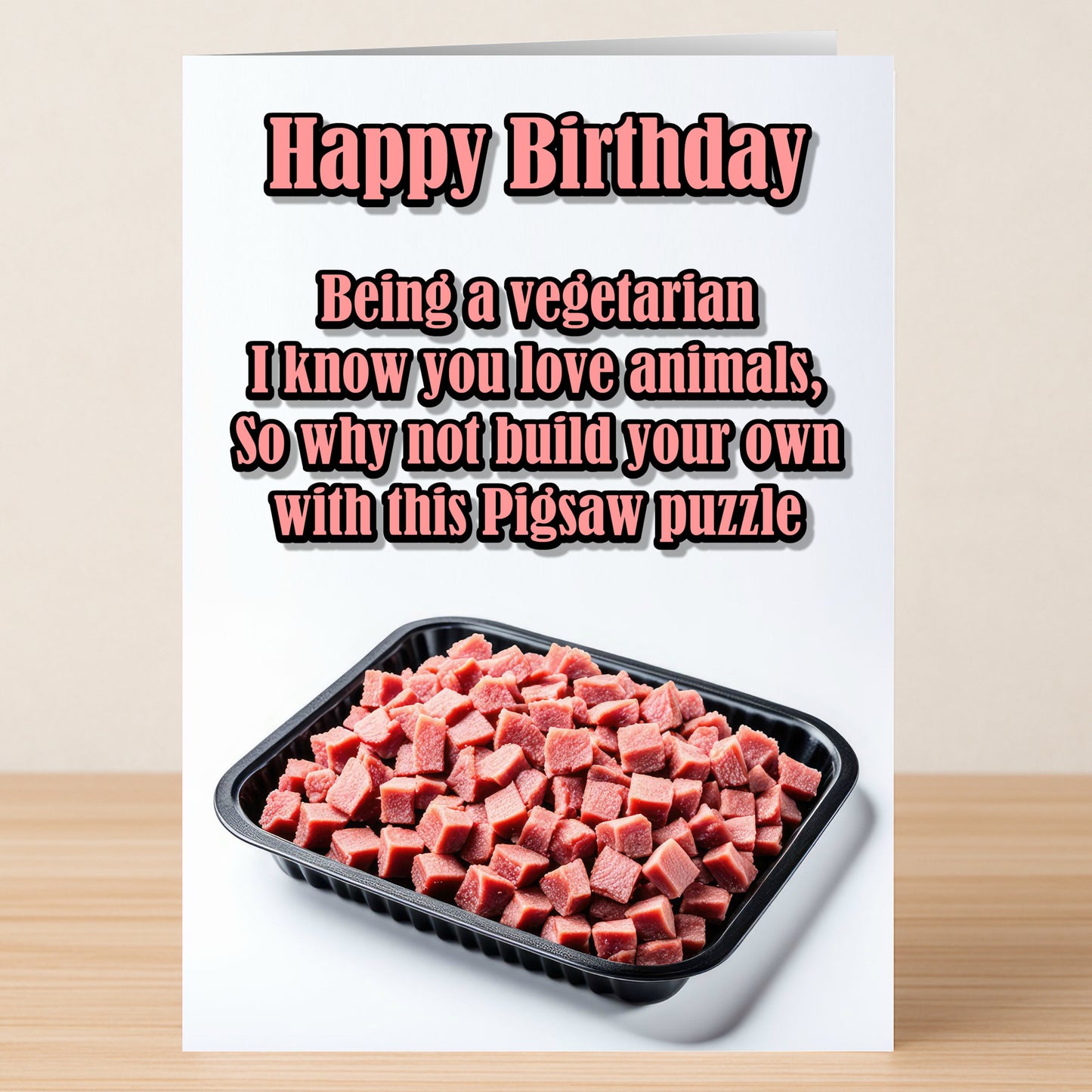 The Twisted Gifts Pigsaw Puzzle – Funny Birthday Card features the message: "Happy Birthday. Being a vegetarian I know you love animals, so why not build your own with this pigsaw puzzle," above a tray of diced meat.