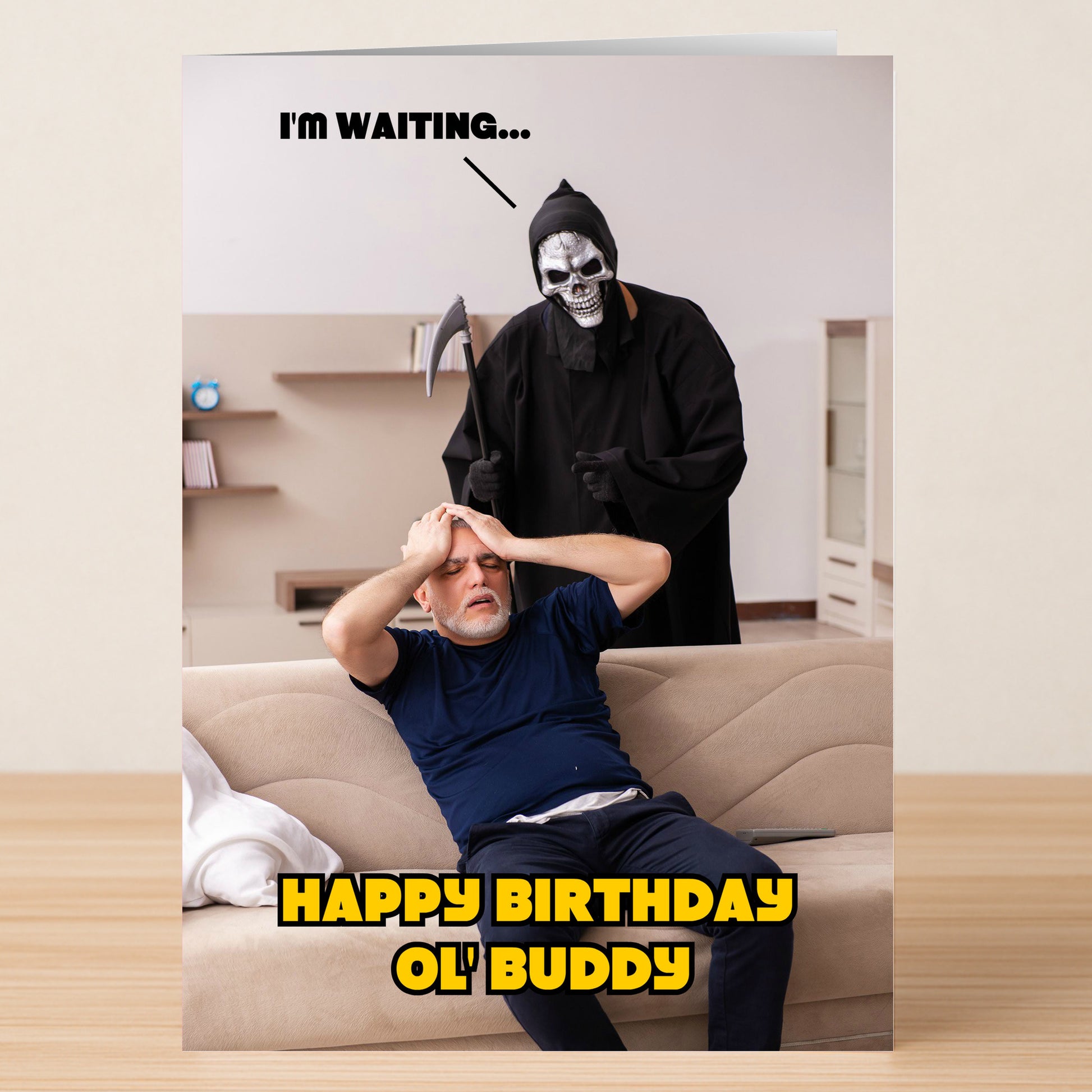 A stressed man sits on a couch as the Grim Reaper looms behind him with "I'M WAITING..." above and bold yellow "HAPPY BIRTHDAY OL' BUDDY" below. Waiting – Funny Birthday Card by Twisted Gifts—ideal for dark humor lovers.