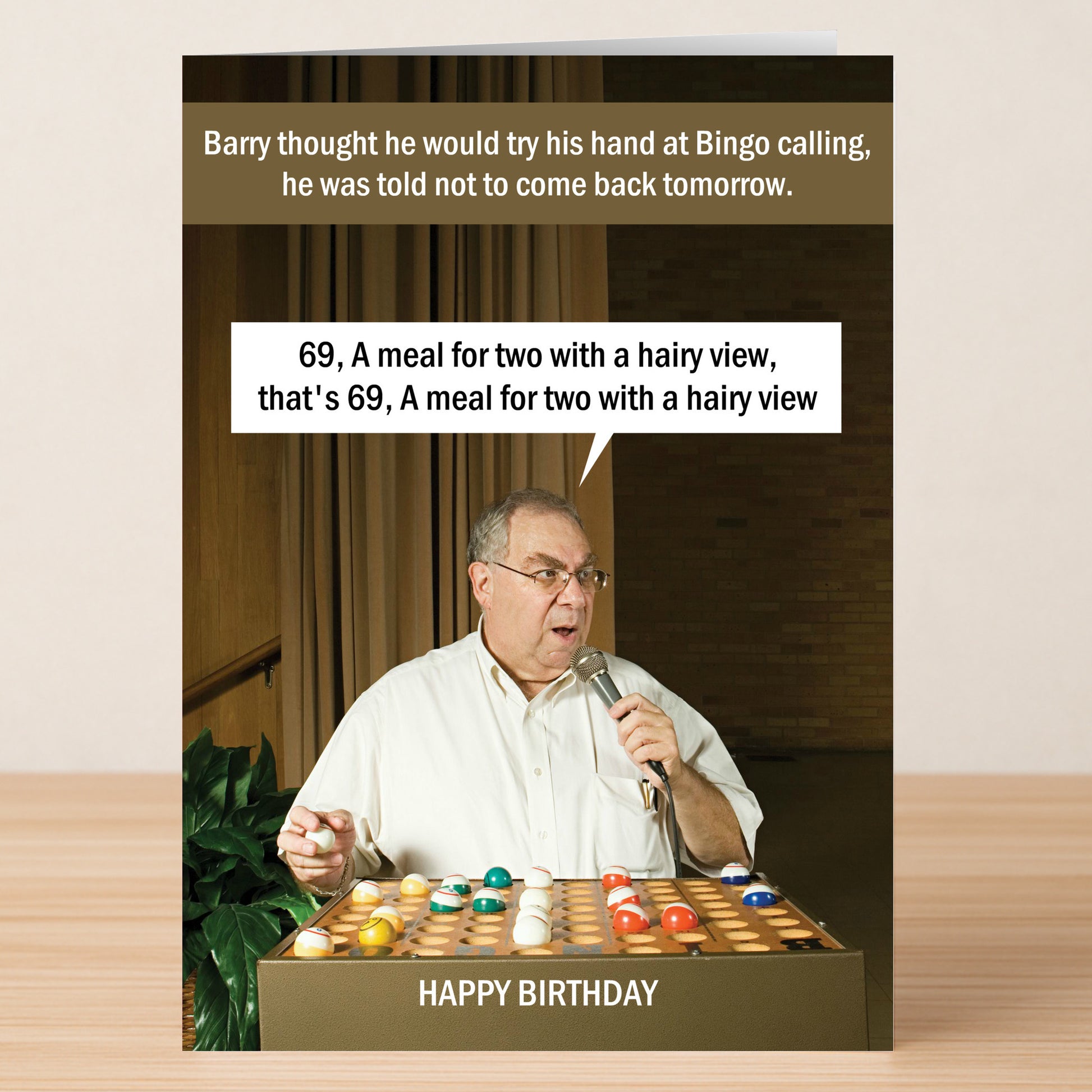 A man calling bingo numbers with a mic stands behind a bingo set; funny rude text above and below him makes this Twisted Gifts "A Meal For 2 – Rude Birthday Card" the perfect hilarious surprise.