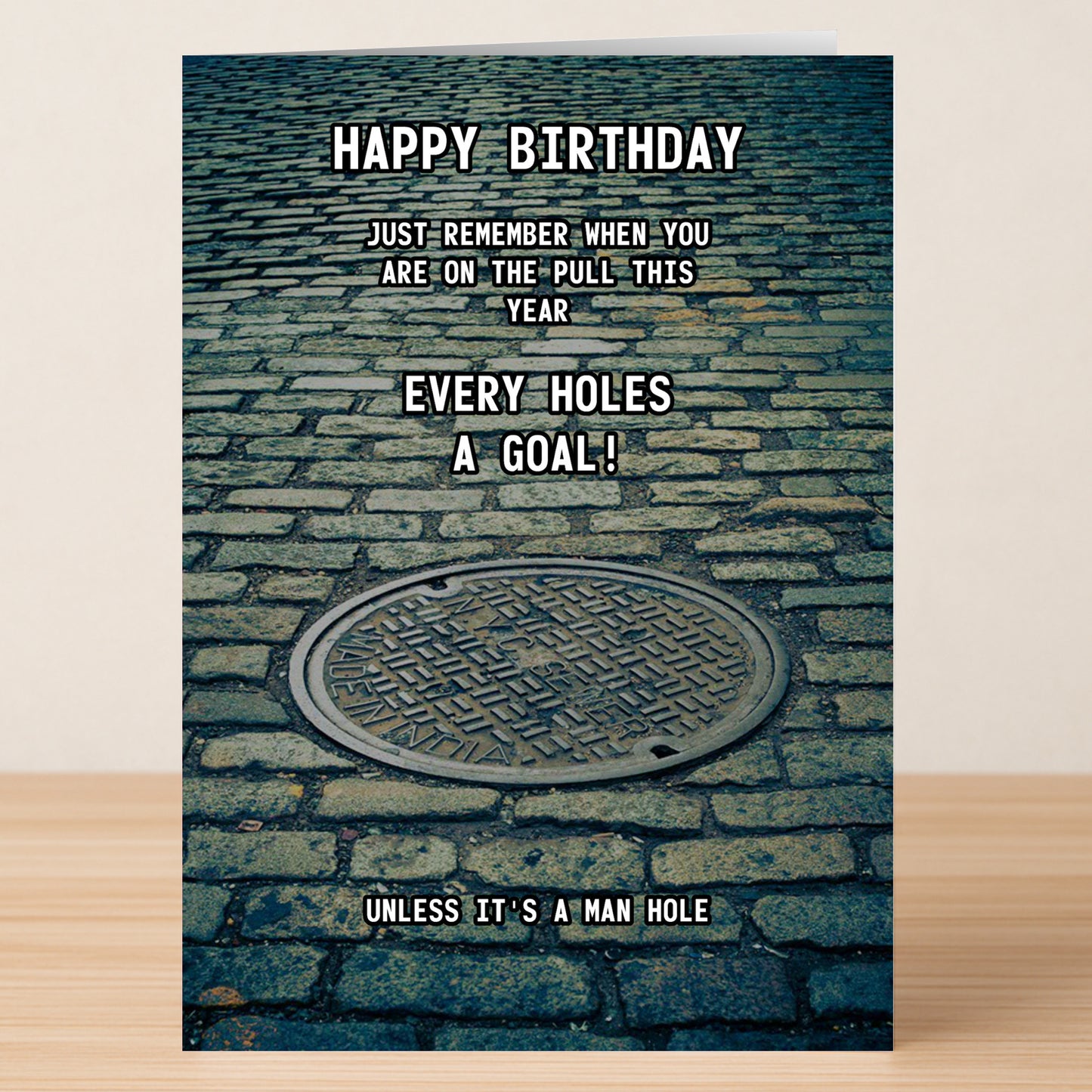 The Man Hole – Rude Birthday Card by Twisted Gifts features a manhole cover on cobblestone and the cheeky message: "Happy Birthday. Just remember when you are on the pull this year every hole's a goal! Unless it's a man hole.