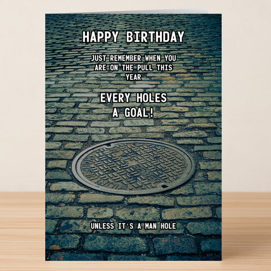 The Man Hole – Rude Birthday Card by Twisted Gifts features a manhole cover on cobblestone and the cheeky message: "Happy Birthday. Just remember when you are on the pull this year every hole's a goal! Unless it's a man hole.